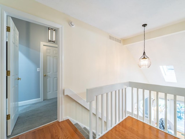hall featuring visible vents, wood finished floors, an upstairs landing, and vaulted ceiling with skylight