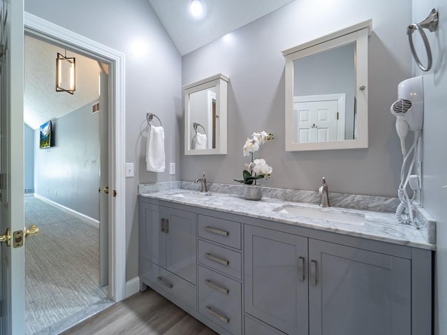 bathroom featuring a sink, double vanity, wood finished floors, and lofted ceiling