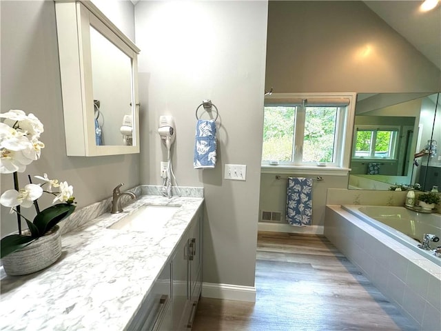 bathroom featuring visible vents, vanity, wood finished floors, baseboards, and a bath