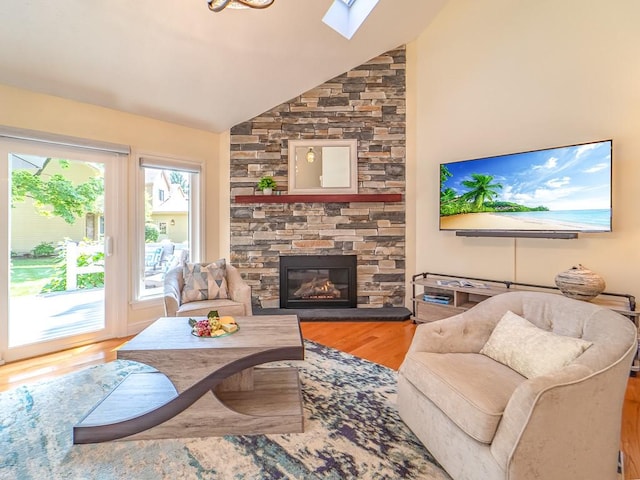 living area featuring vaulted ceiling with skylight, a stone fireplace, and wood finished floors