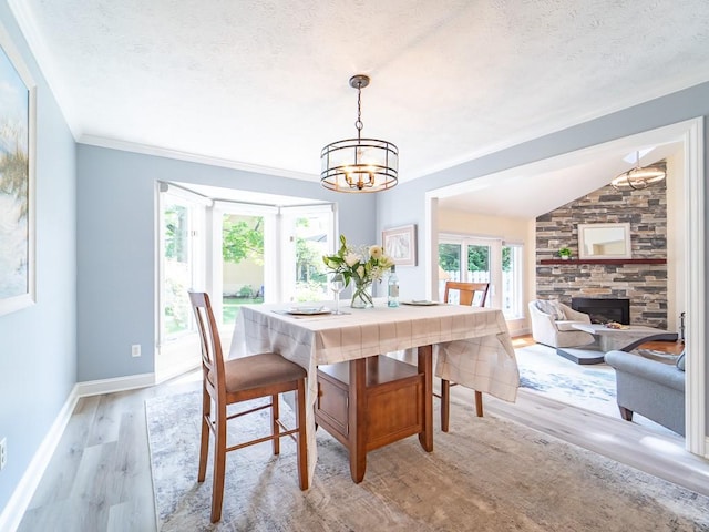 dining room with a textured ceiling, a fireplace, light wood-type flooring, baseboards, and a chandelier