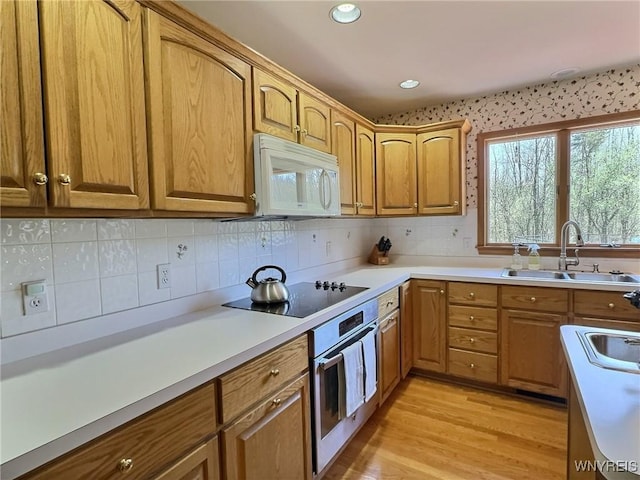 kitchen with a sink, oven, white microwave, light countertops, and black electric stovetop
