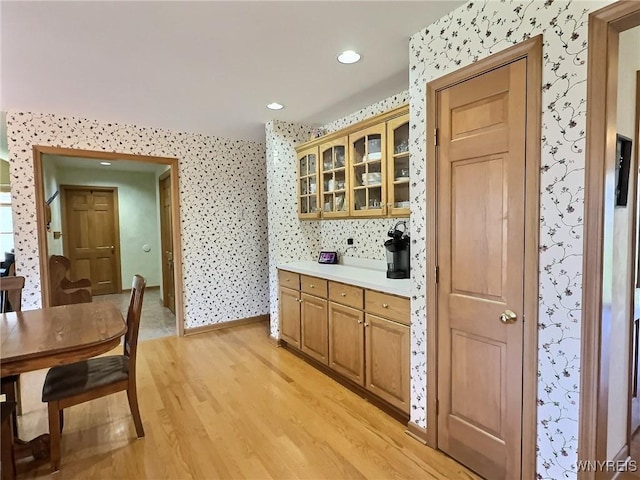 kitchen with light wood finished floors, glass insert cabinets, light countertops, and wallpapered walls