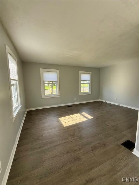 empty room featuring baseboards, dark wood-style flooring, and visible vents