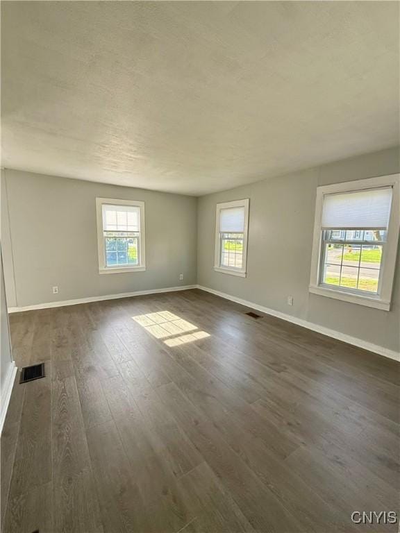 spare room featuring baseboards, visible vents, dark wood-style floors, and a healthy amount of sunlight