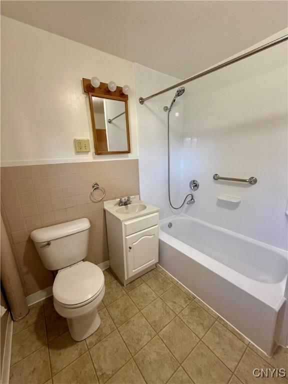 bathroom featuring tile patterned flooring, a wainscoted wall, vanity, toilet, and shower / bathtub combination