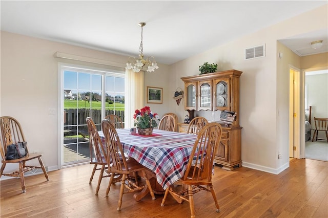 dining space featuring baseboards, light wood-type flooring, a chandelier, and visible vents