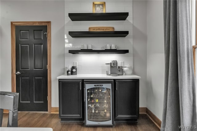 bar with beverage cooler, baseboards, dark wood-type flooring, a dry bar, and backsplash