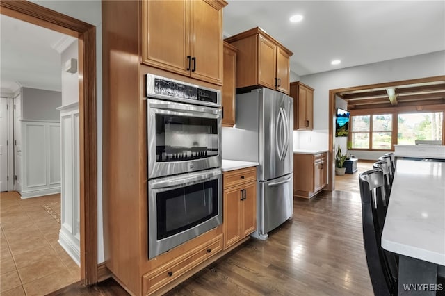 kitchen with ornamental molding, dark wood-type flooring, recessed lighting, brown cabinets, and appliances with stainless steel finishes