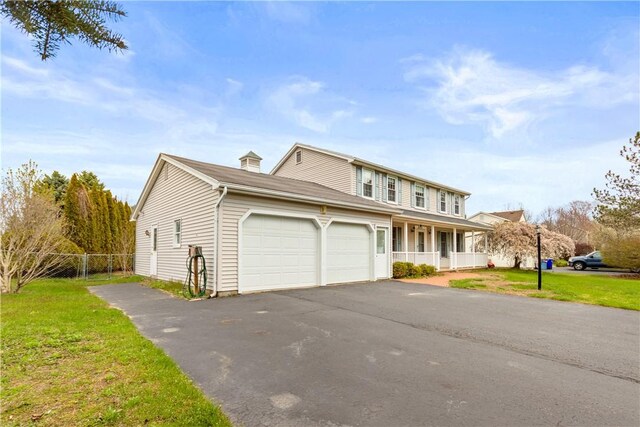 traditional-style house featuring aphalt driveway, fence, a front lawn, and a garage