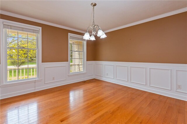 spare room featuring light wood-style floors, ornamental molding, a wainscoted wall, and a notable chandelier