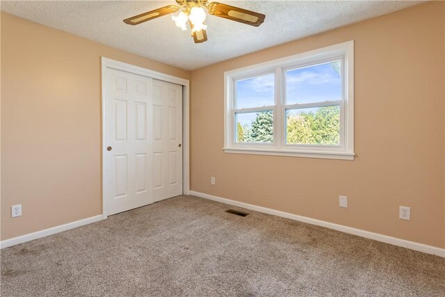 unfurnished bedroom with carpet floors, a textured ceiling, baseboards, visible vents, and a closet