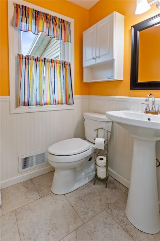 half bathroom with visible vents, a sink, a wainscoted wall, and toilet