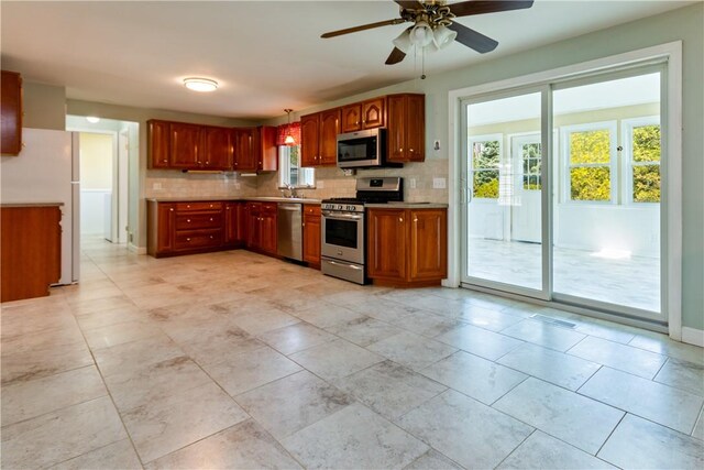 kitchen with a sink, light countertops, tasteful backsplash, a ceiling fan, and appliances with stainless steel finishes