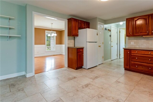 kitchen with an inviting chandelier, light countertops, freestanding refrigerator, and backsplash