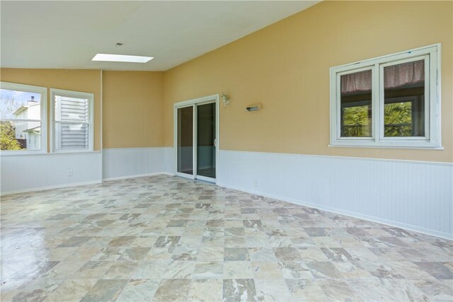 empty room with a wainscoted wall, lofted ceiling with skylight, and stone finish flooring