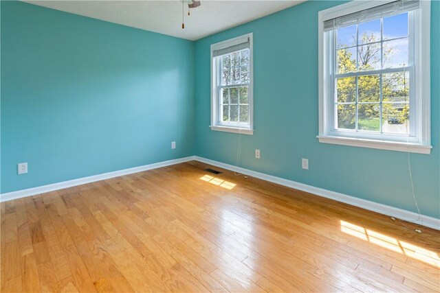 empty room featuring a ceiling fan, baseboards, visible vents, and light wood finished floors