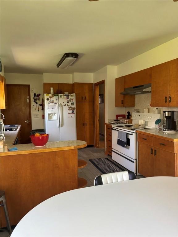 1001 W Broad St, Horseheads, NY 14845 - kitchen with white appliances, under cabinet range hood, brown cabinetry, and light countertops