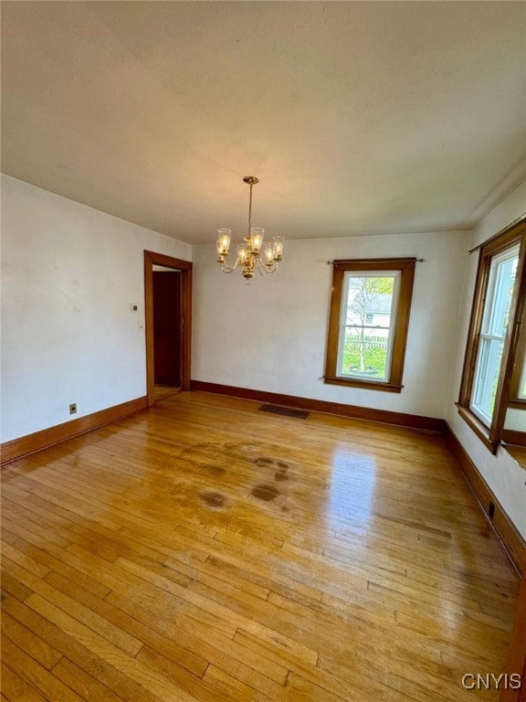 spare room with baseboards, light wood-type flooring, a chandelier, and visible vents