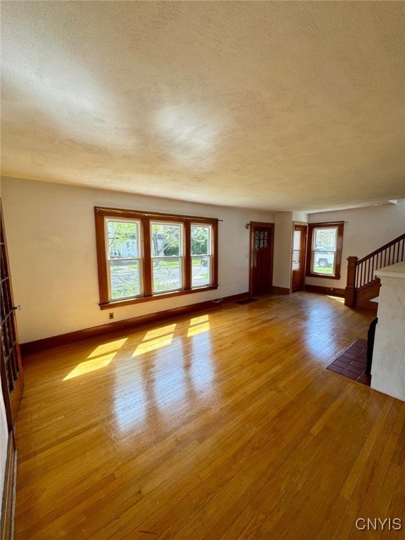unfurnished living room with baseboards, a textured ceiling, wood finished floors, and a wealth of natural light