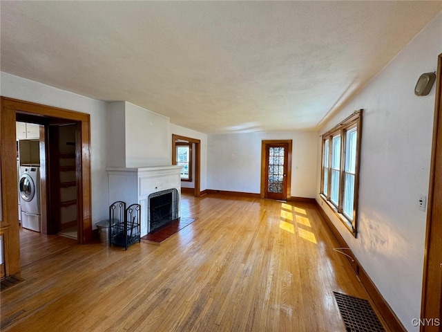 unfurnished living room with light wood-style floors, a fireplace with raised hearth, washer / clothes dryer, baseboards, and visible vents