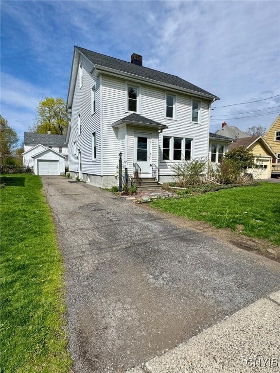 view of front of home with a front lawn, aphalt driveway, a chimney, entry steps, and a detached garage