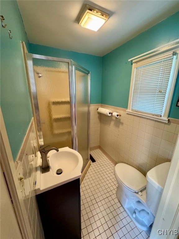 bathroom with wainscoting, tile walls, a shower stall, and toilet