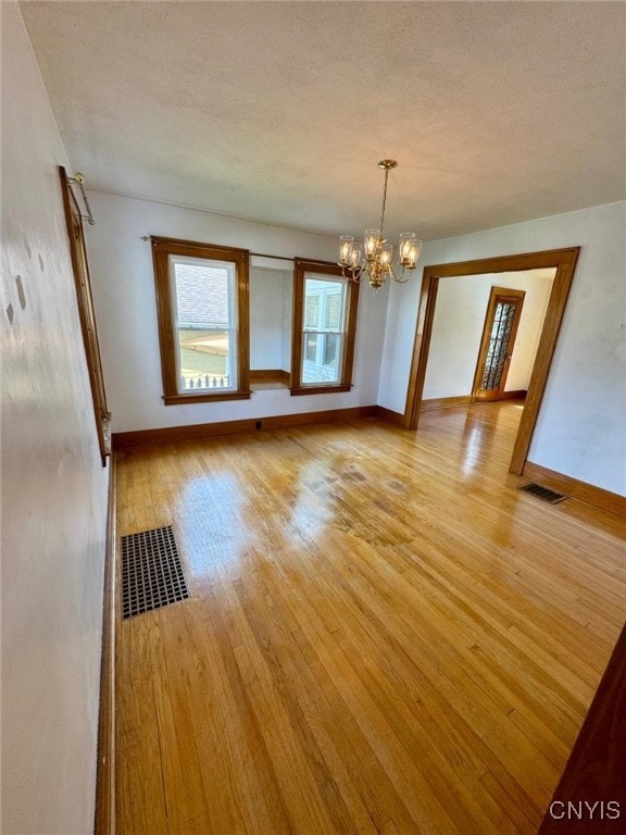 unfurnished dining area featuring baseboards, light wood finished floors, a chandelier, and visible vents