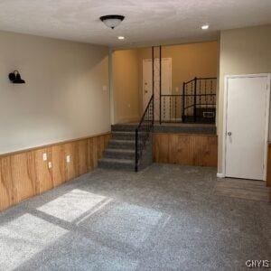 134 Malden Rd, Salina, NY 13211 - unfurnished living room with stairs, wooden walls, carpet, and a wainscoted wall