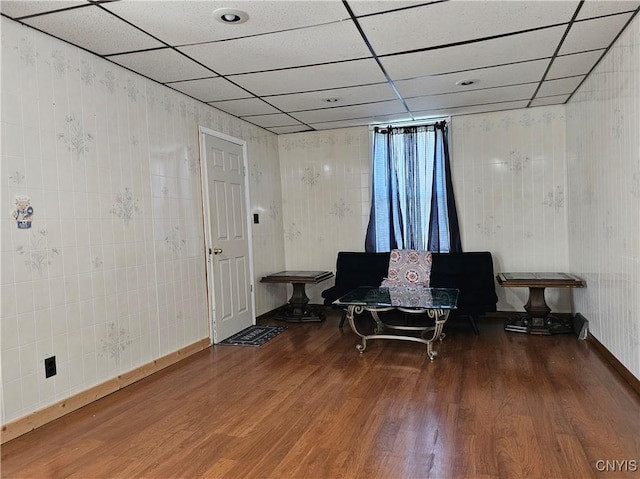 sitting room featuring baseboards, a drop ceiling, and wood finished floors
