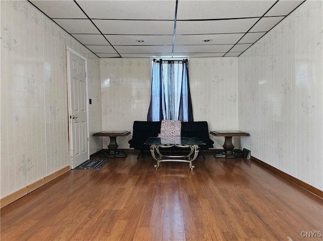 living area featuring baseboards, a drop ceiling, and wood finished floors