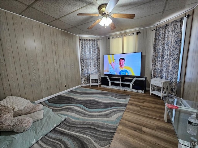 home theater room with wood walls, wood finished floors, baseboards, a paneled ceiling, and a ceiling fan