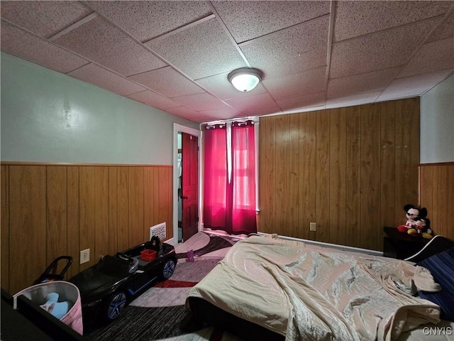 bedroom featuring wooden walls, visible vents, a drop ceiling, and a wainscoted wall