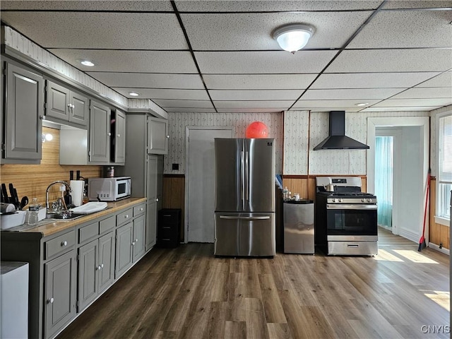 kitchen featuring wall chimney range hood, dark wood-style flooring, appliances with stainless steel finishes, and gray cabinets