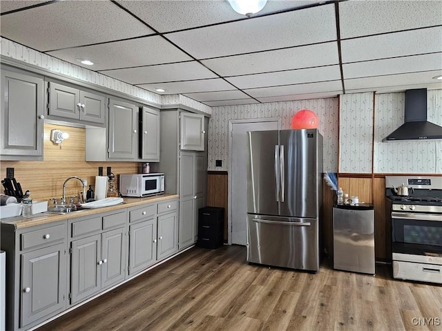 kitchen featuring gray cabinetry, appliances with stainless steel finishes, wallpapered walls, and wall chimney exhaust hood