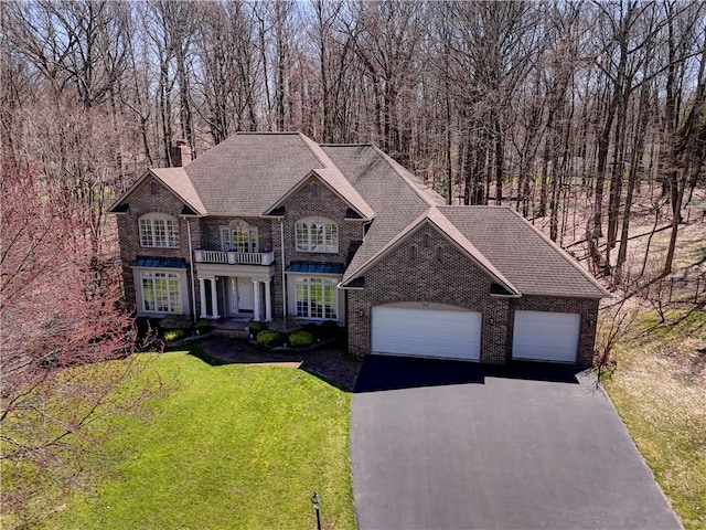 view of front of home featuring aphalt driveway, a chimney, brick siding, a balcony, and a front lawn