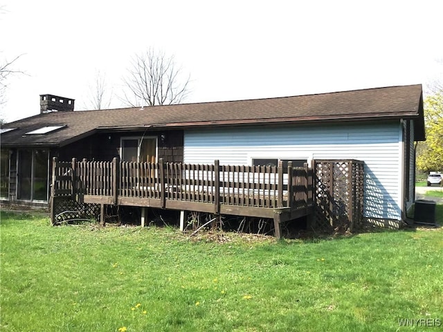 back of property featuring a lawn, a shingled roof, a chimney, and a deck