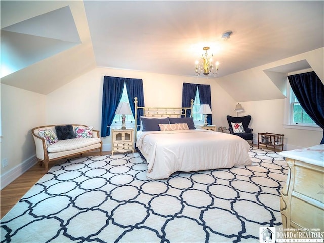 bedroom featuring wood finished floors, baseboards, lofted ceiling, and a notable chandelier