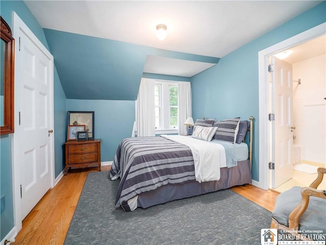 bedroom with baseboards, vaulted ceiling, and light wood-style flooring