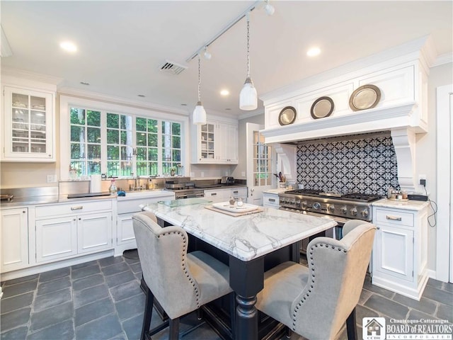 kitchen with stainless steel gas range oven, white cabinets, a kitchen breakfast bar, and visible vents