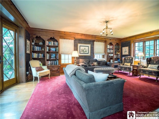 living area with ornamental molding, wooden walls, a notable chandelier, and built in shelves