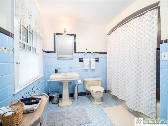 full bath featuring tile patterned flooring, toilet, tile walls, a wainscoted wall, and a sink