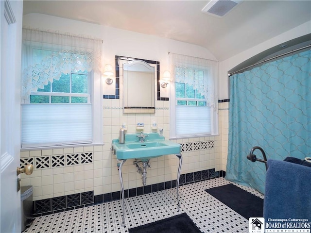 full bathroom with tile walls, a wealth of natural light, a shower with shower curtain, and visible vents