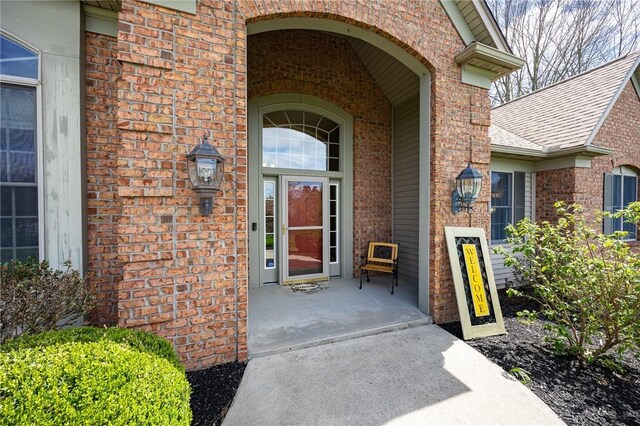 entrance to property with a porch, brick siding, and a shingled roof
