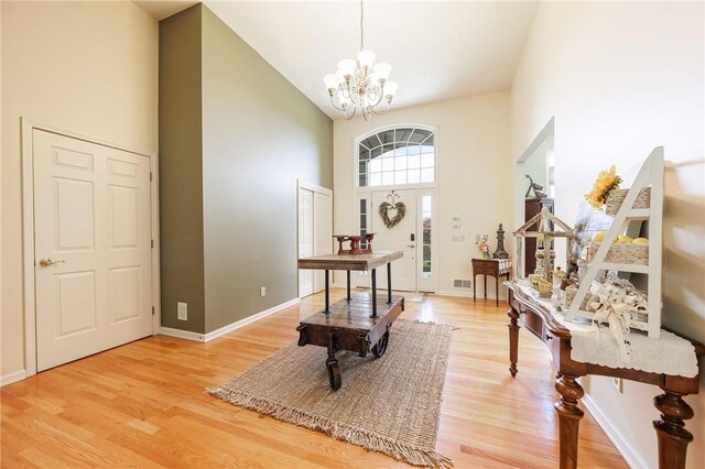 foyer entrance featuring high vaulted ceiling, baseboards, light wood finished floors, and a notable chandelier