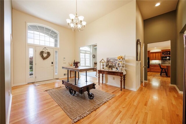foyer entrance featuring an inviting chandelier, light wood-style flooring, and a high ceiling