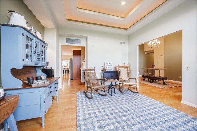 sitting room with visible vents, light wood finished floors, a tray ceiling, and a chandelier