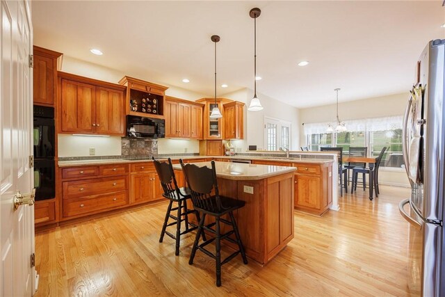 kitchen with a peninsula, light wood-style floors, black appliances, and a center island