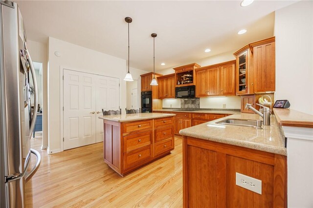 kitchen featuring decorative light fixtures, light wood-type flooring, brown cabinets, a sink, and black appliances