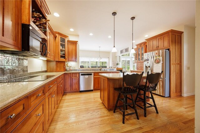 kitchen featuring a kitchen breakfast bar, light wood-type flooring, black appliances, and brown cabinets